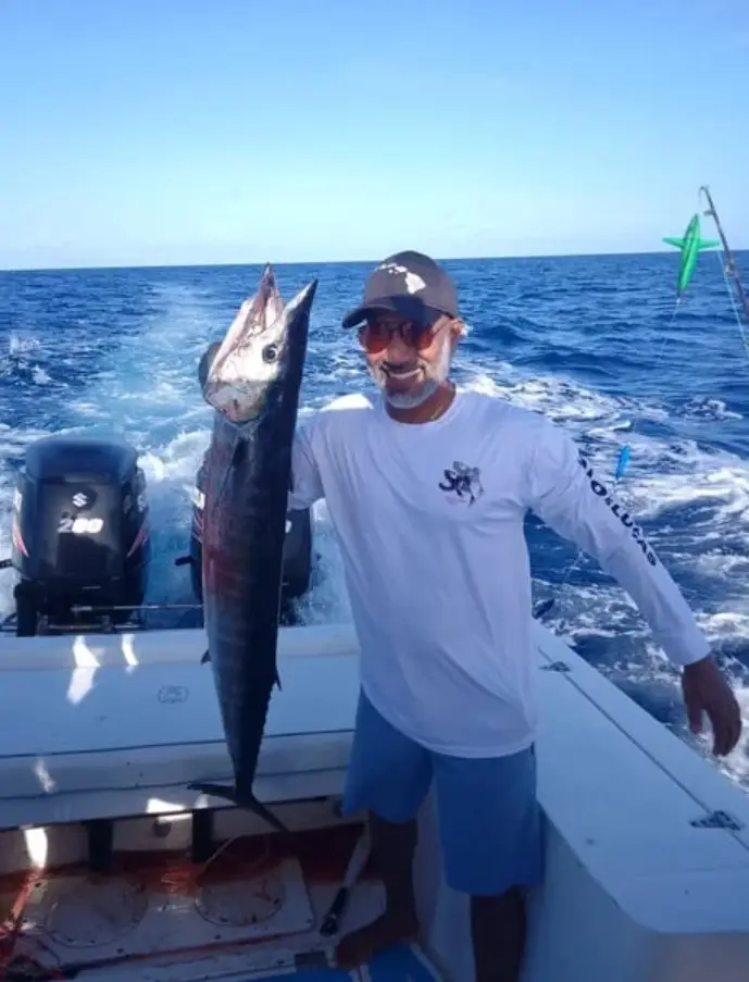 Guest with big smile holding a large wahoo aboard Dos Reyes Roatan deep sea fishing charter in the Caribbean