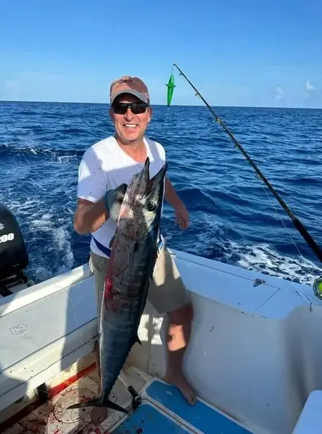Happy guest holding a large wahoo aboard Dos Reyes Roatan deep sea fishing charter in the Caribbean