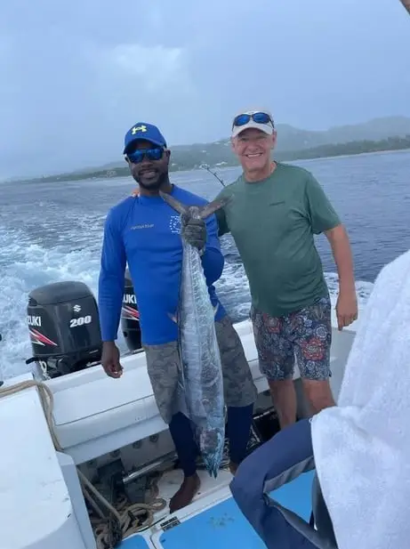 Captain Julio and guest holding a large wahoo aboard Dos Reyes Roatan deep sea fishing charter in the Caribbean