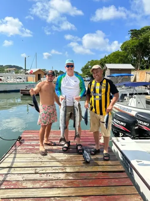 Three friends holding blackfin tuna and barracuda aboard Dos Reyes Roatan deep sea fishing charter in the Caribbean