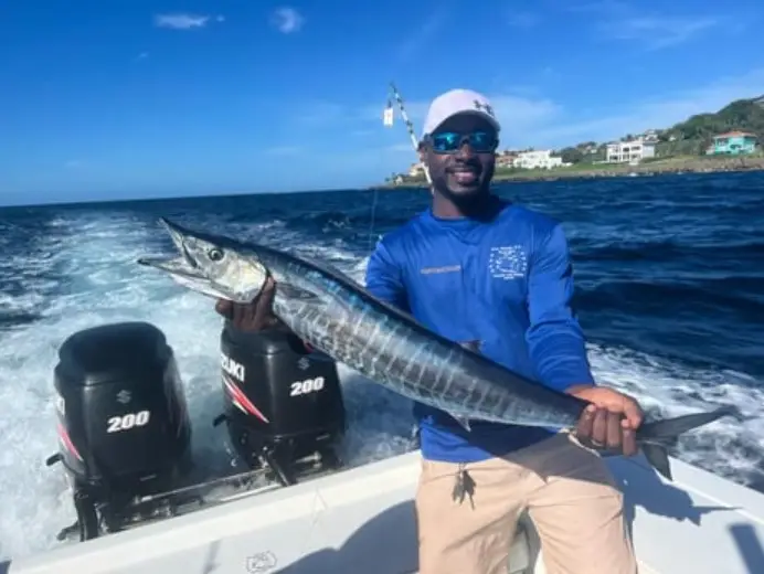 Captain Julio holding a large wahoo aboard Dos Reyes Roatan deep sea fishing charter in the Caribbean