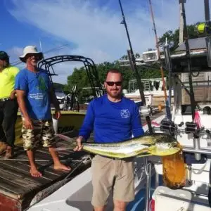 Chip holding a freshly caught mahi mahi aboard Dos Reyes Roatan — deep sea fishing charter in the Caribbean landing vibrant dorado on turquoise waters