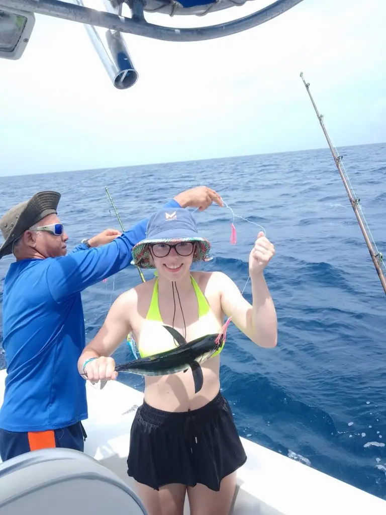 Happy daughter holding a freshly caught Blackfin Tuna while First Mate Eddie fixes the fishing line aboard Dos Reyes Roatan — family-friendly deep sea fishing charter in the Caribbean