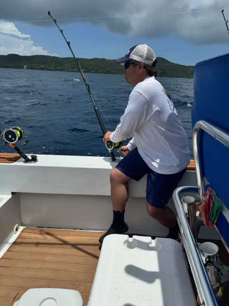 Man reeling in fish on Dos Reyes Roatan Charter — private deep sea fishing tour in Caribbean waters targeting Wahoo, Tuna, and Mahi-Mahi